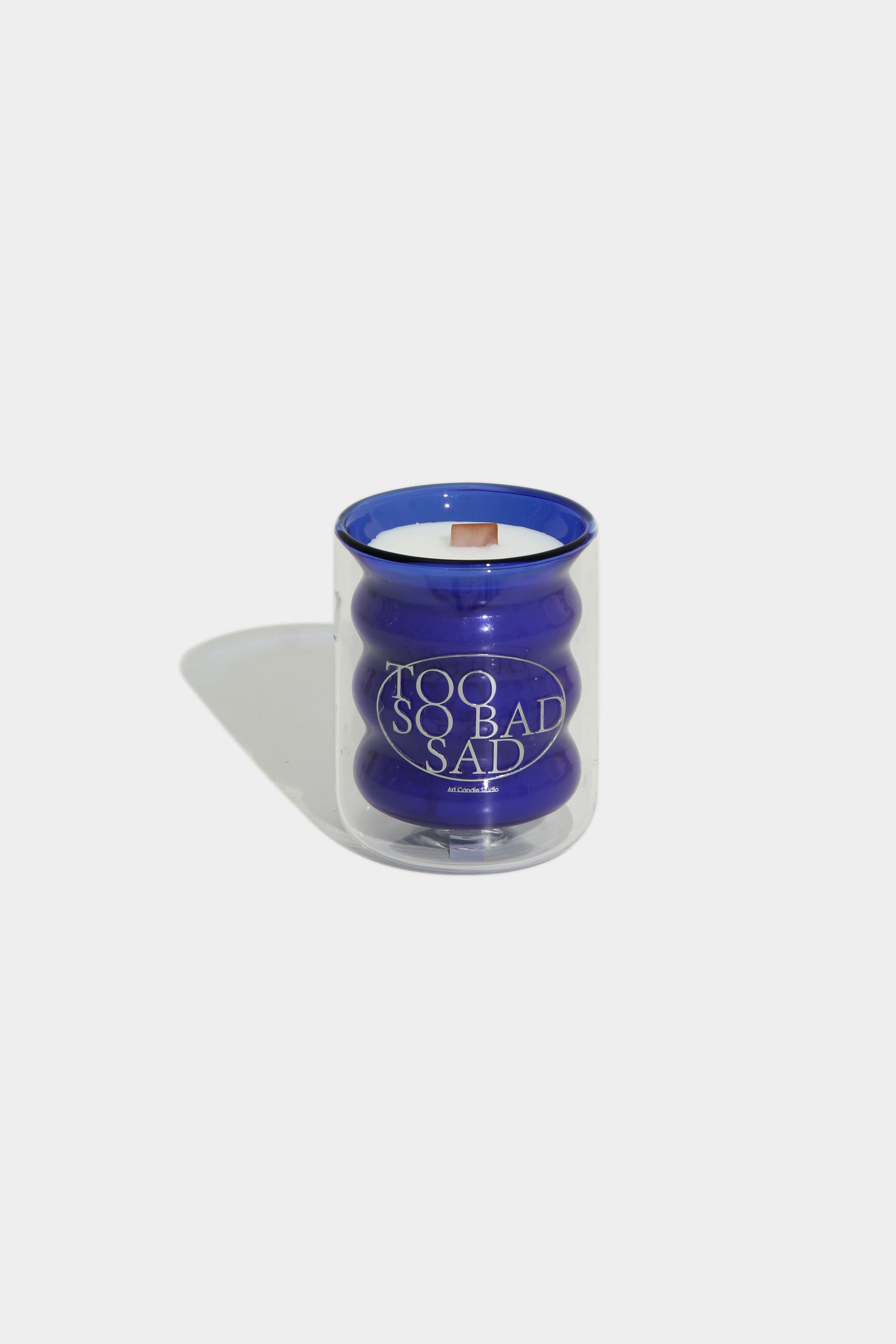 Candle with 'Too So Bad Sad' text on a white background
