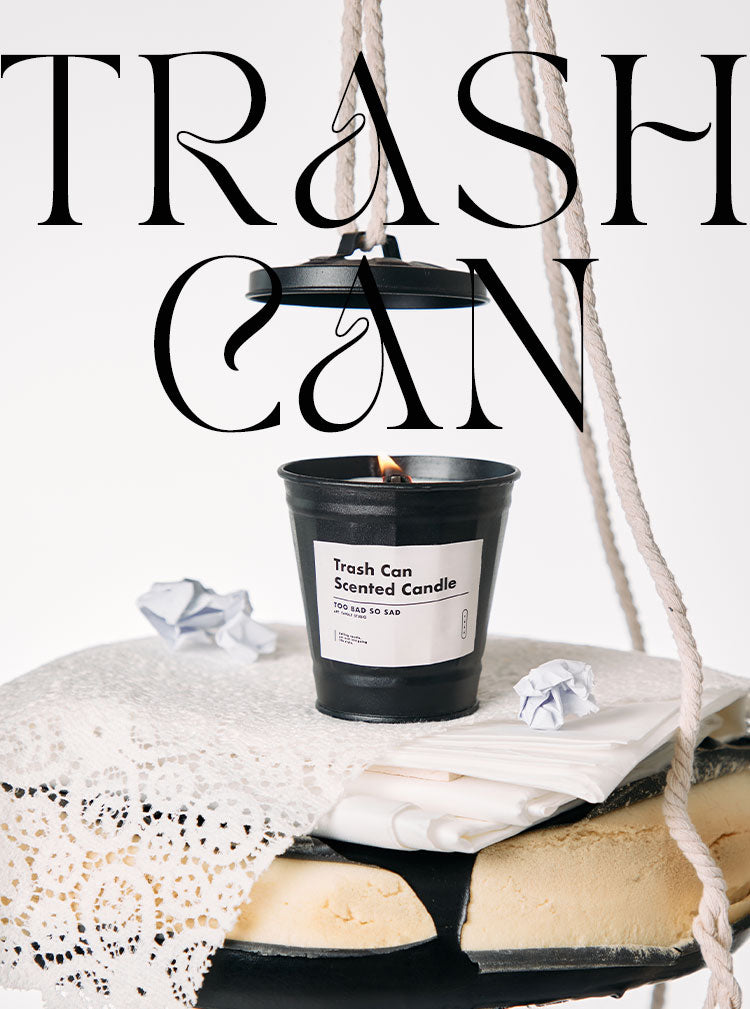 Black trash can-shaped candle with crumpled paper on a white surface