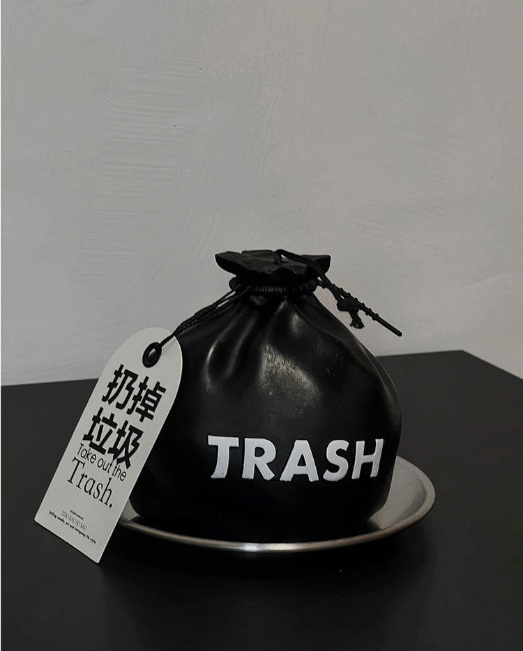 Black drawstring bag labeled 'TRASH' with a tag on a dark surface.