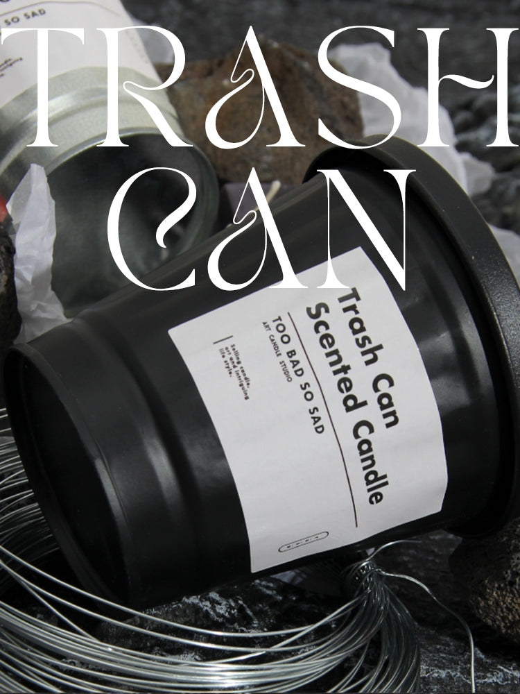 Black candle labeled 'Trash Can Scented Candle' with a label reading 'Too Bad So Sad' on a dark background.