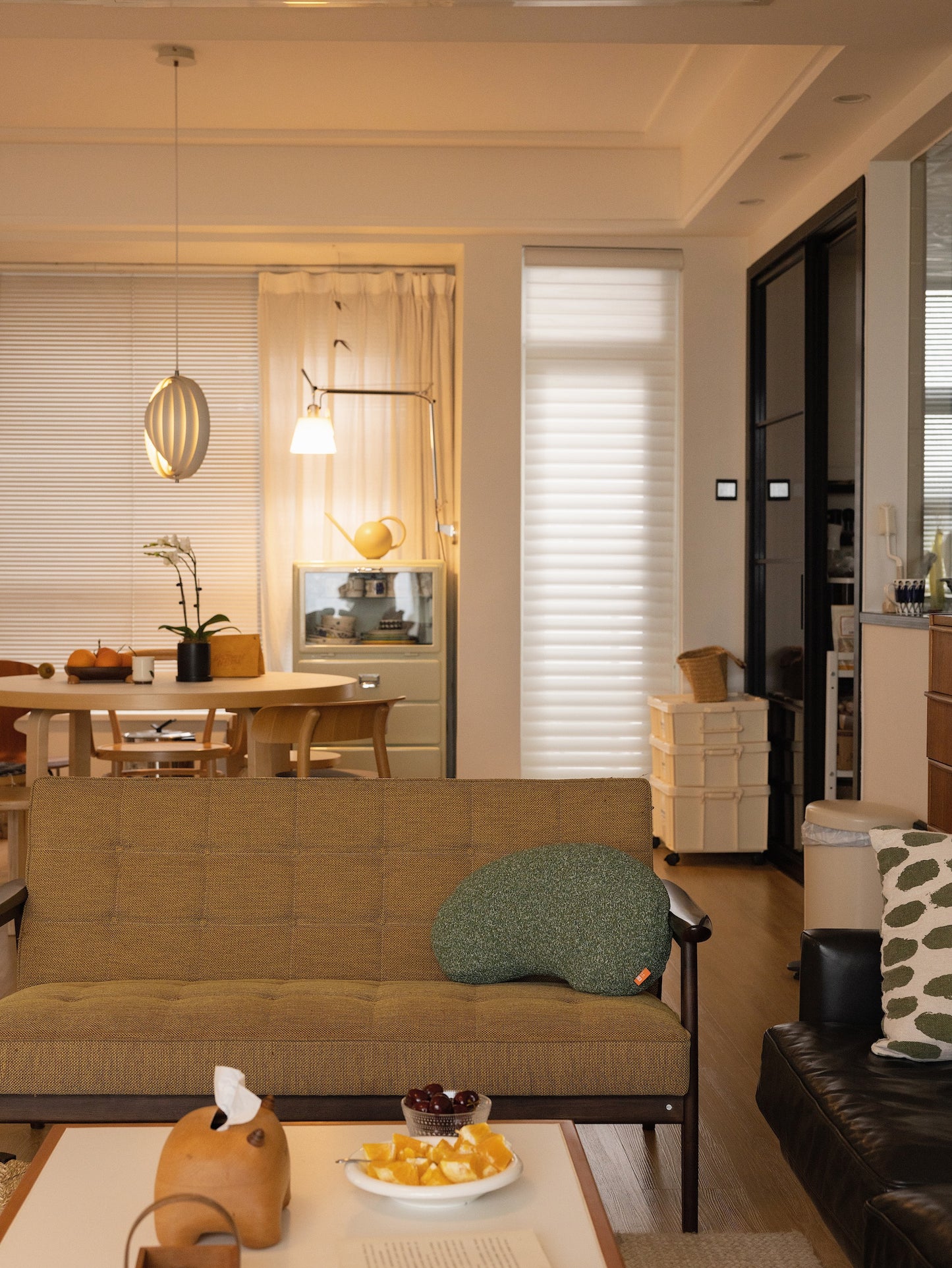 Modern living room with a brown sofa, green pillow, and a view of a kitchen.