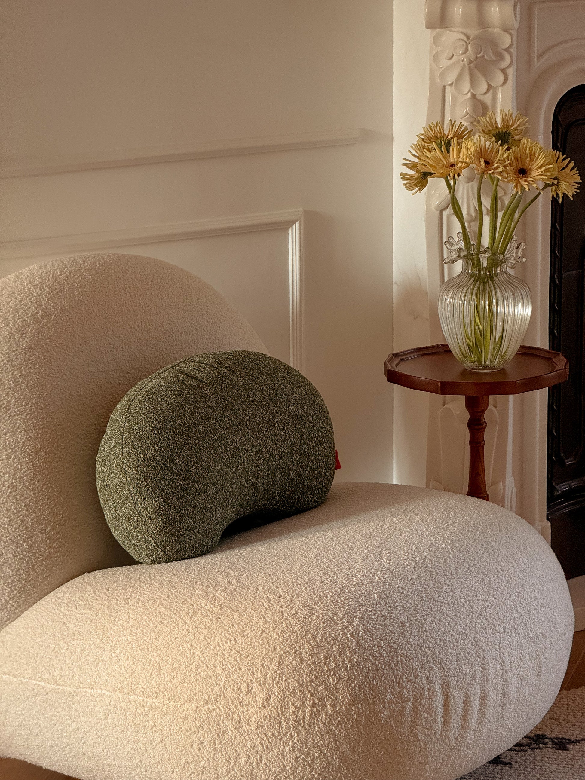 White textured armchair with a green cushion next to a small wooden table with a vase of yellow flowers.