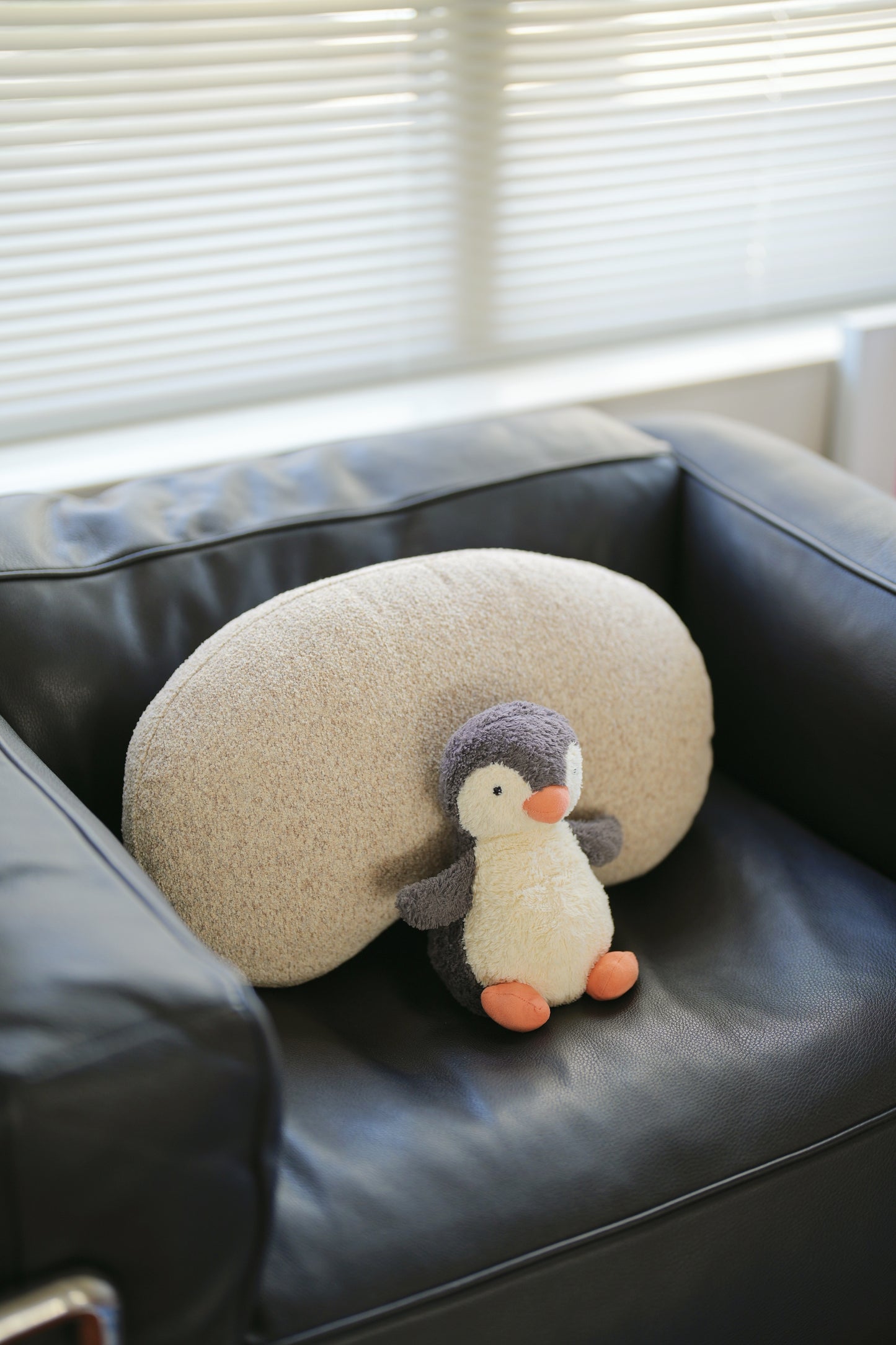 Round pillow with a penguin design on a black leather chair.