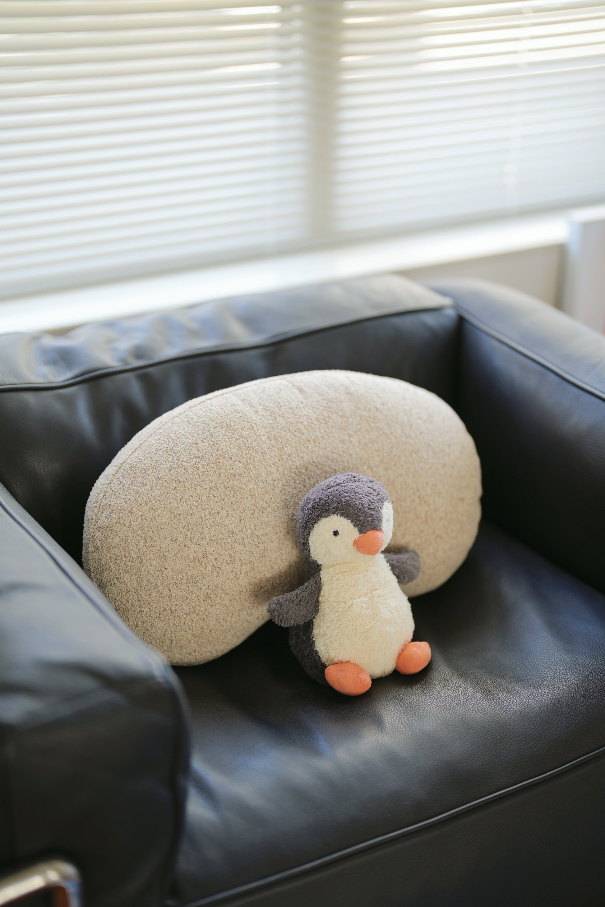 Round pillow with a penguin design on a black leather chair.