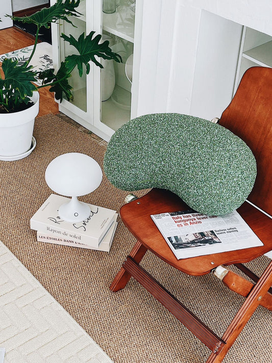 Green cushion on a wooden chair with a book and plant in the background