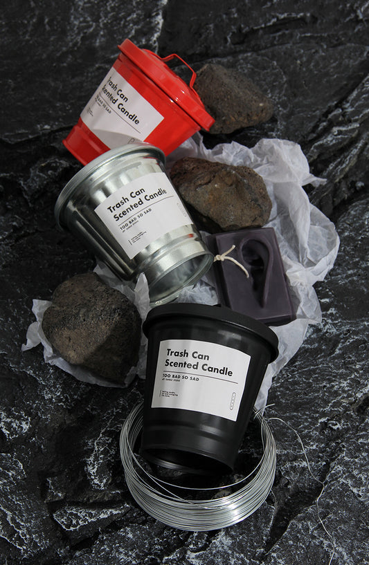 Trash can scented candles on a dark stone surface