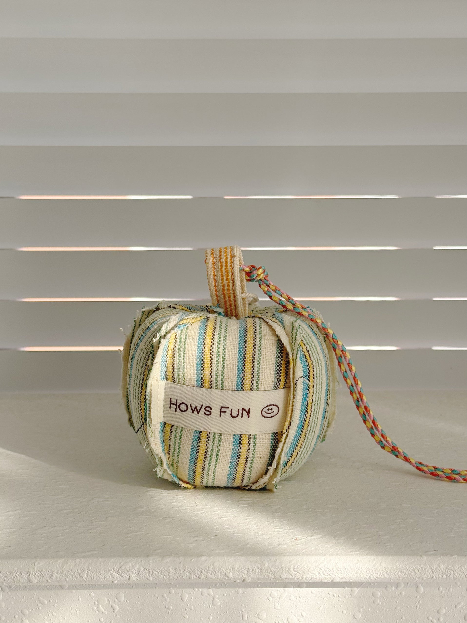 Striped fabric heart-shaped toy with a tag on a neutral background
