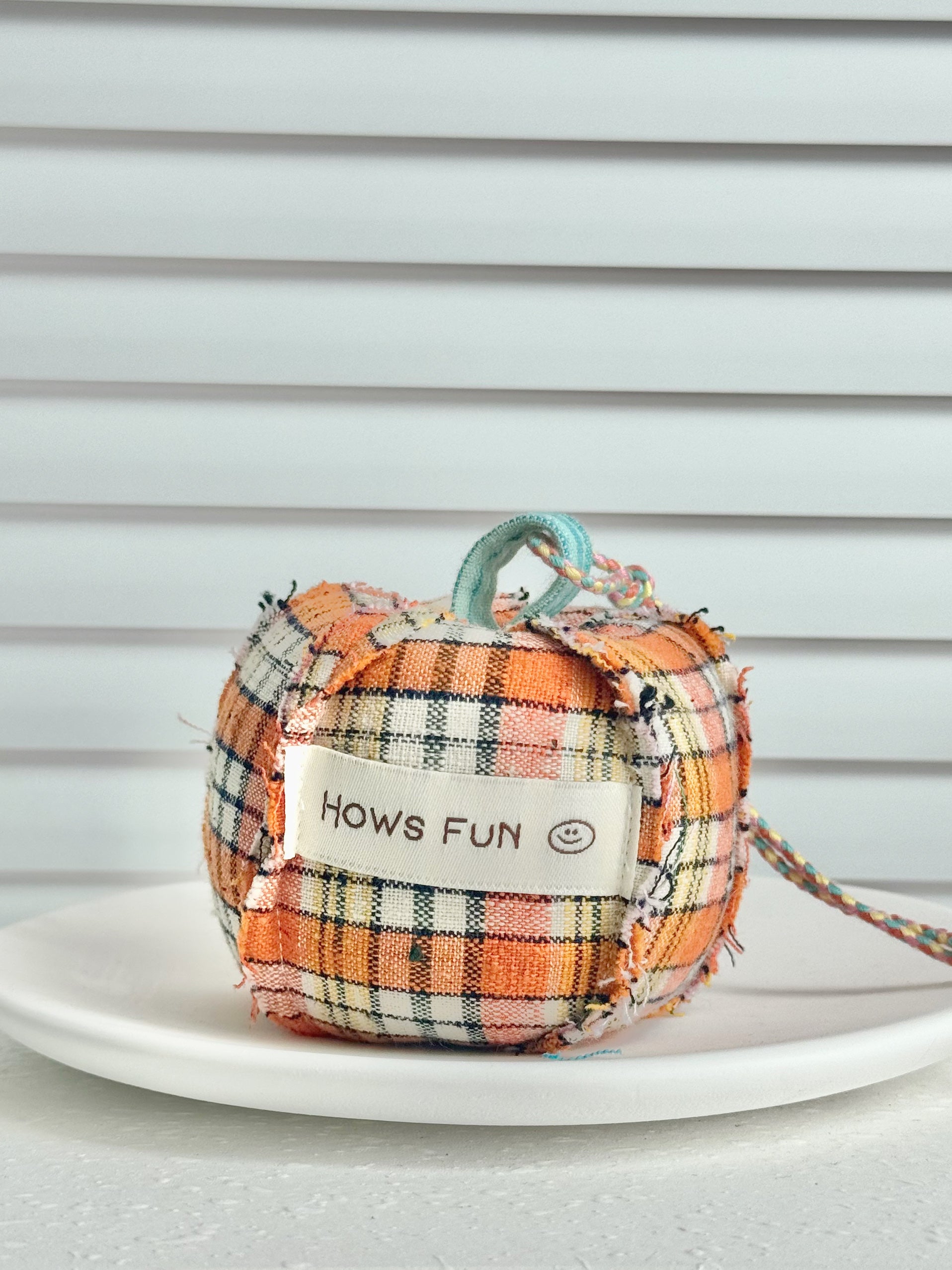 Plaid fabric pumpkin with a tag saying 'Hows fun' on a white surface.