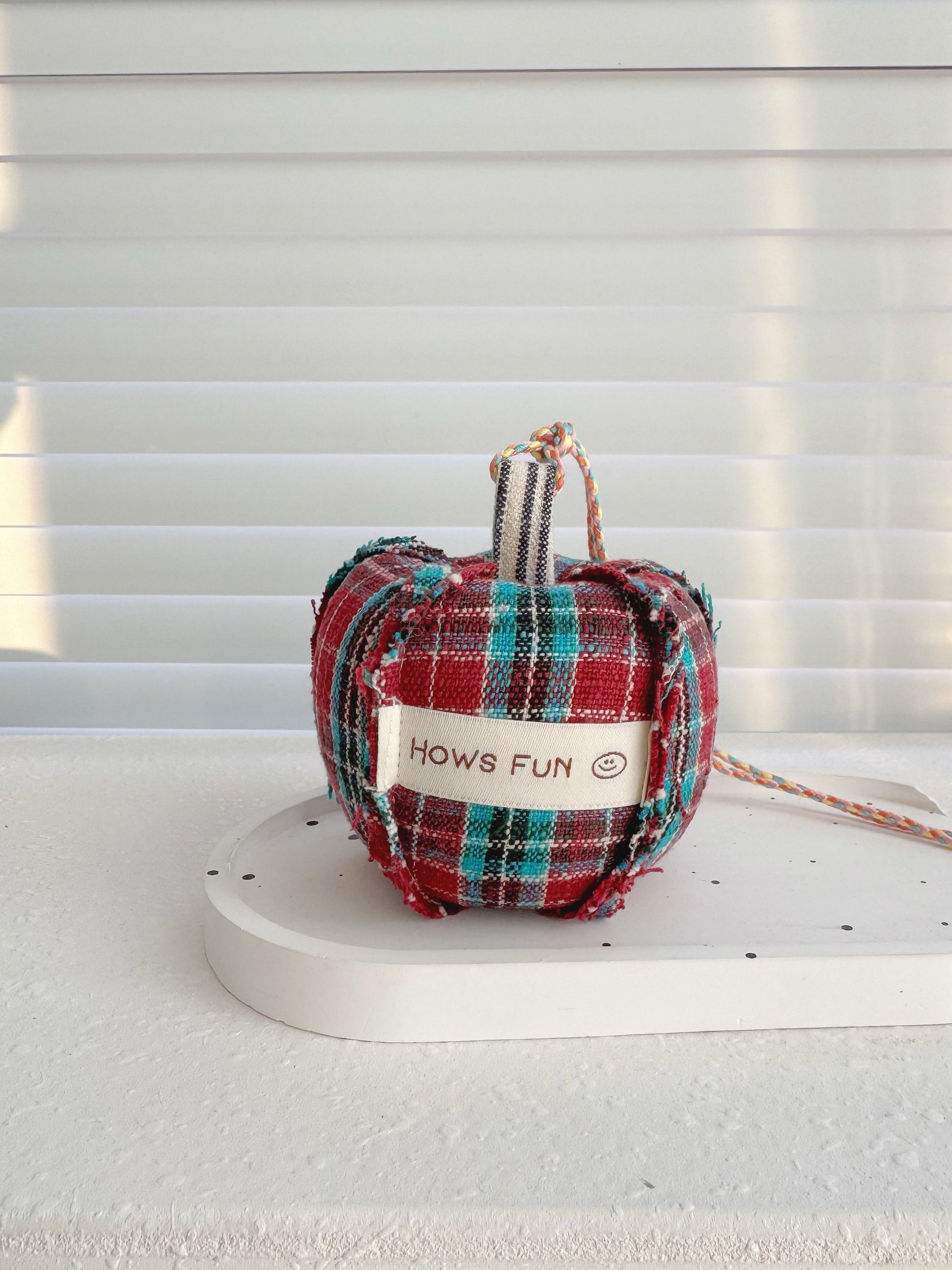 Plaid dog toy shaped like an apple on a white surface with a light gray background