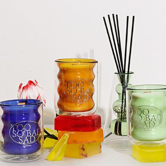 Collection of colorful candles and diffusers with 'Too So Bad' branding on a white background.
