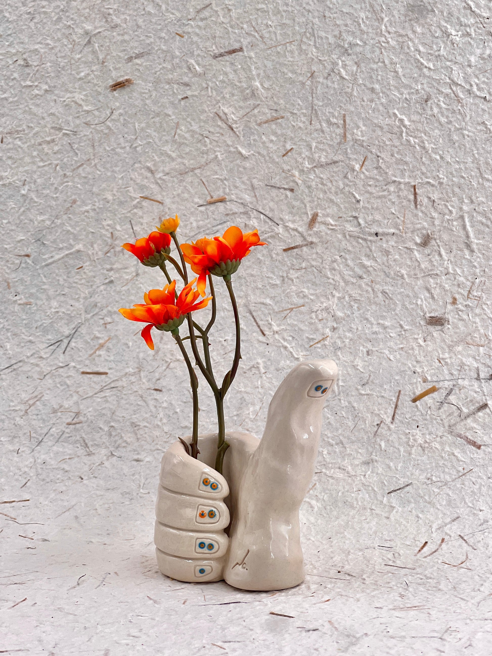 Ceramic hand-shaped vase with orange flowers on a textured gray background