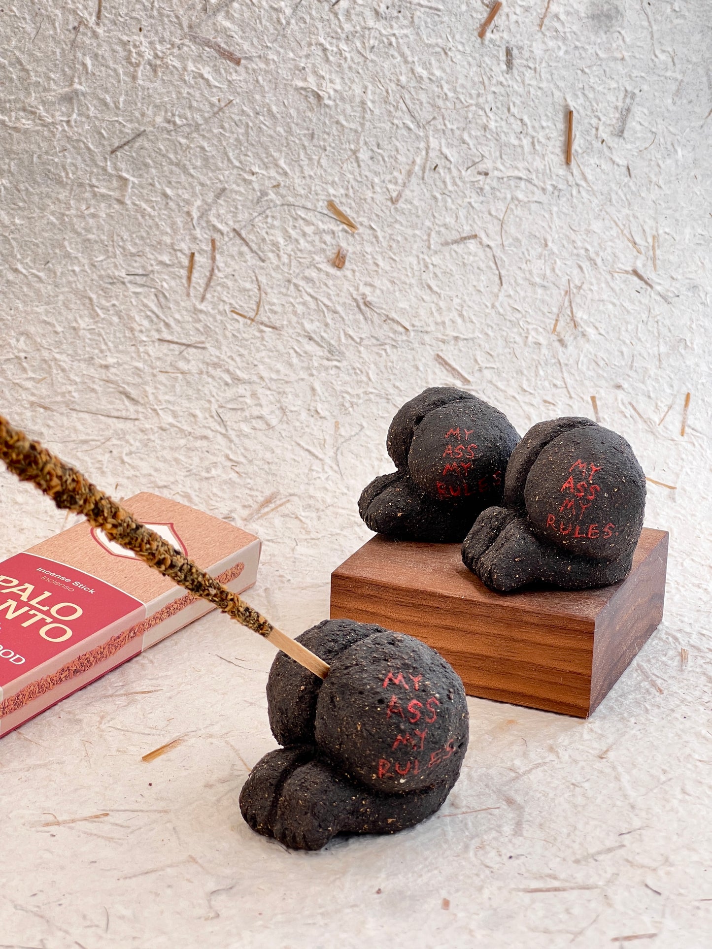Decorative black stone figures on a wooden block with a Palo Santo box on a textured surface.