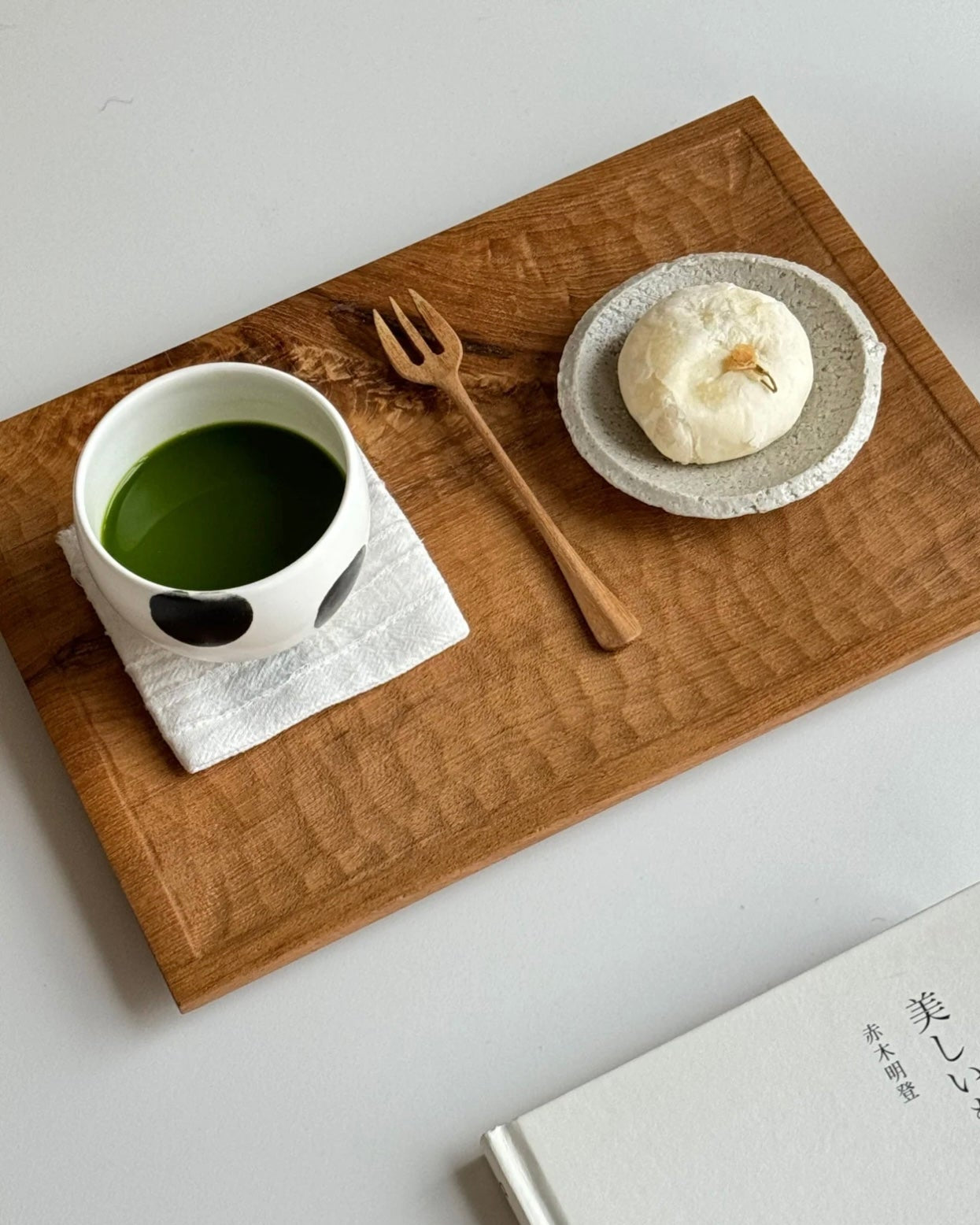 Tea cup with green tea, small plate with a dessert, and fork on a wooden tray with 'VAST' branding.