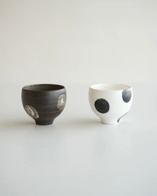 Two ceramic cups, one black and one with white base and black dots, on a light gray background.