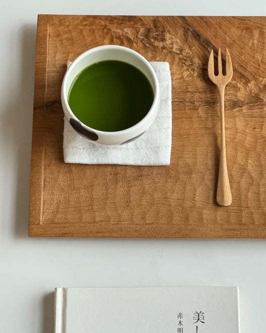 Cup of green tea on a wooden tray with a fork and a book titled 'VAST'.