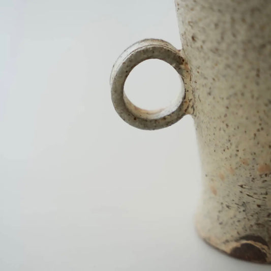Close-up of a ceramic mug with a speckled texture on a light gray background