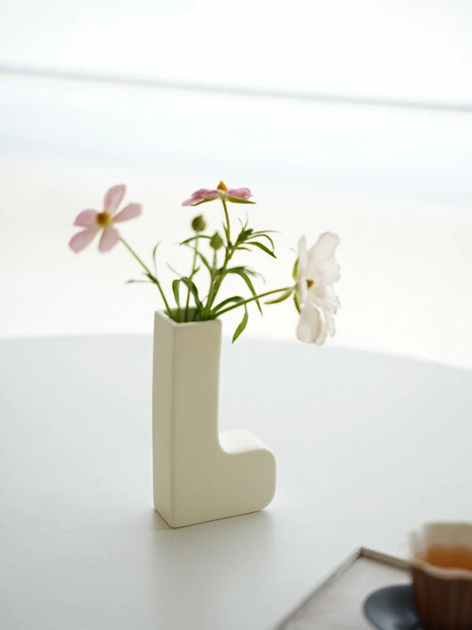 White letter 'L' vase with flowers on a light surface
