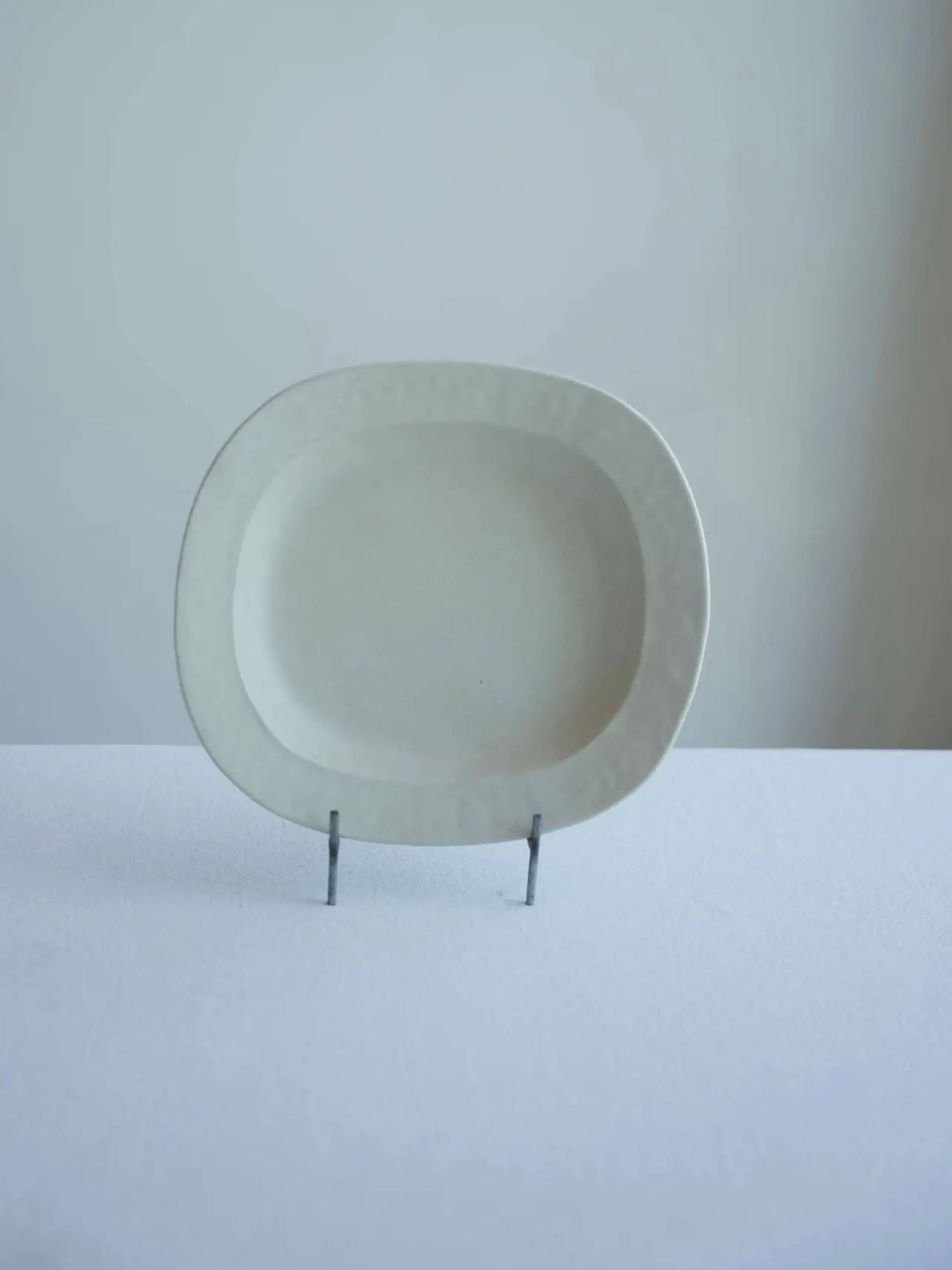 White ceramic plate on a stand against a plain background