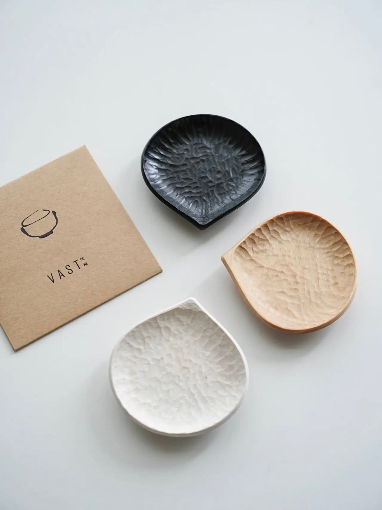 Three ceramic dishes in black, white, and beige on a white surface with a 'VAST' branded card.