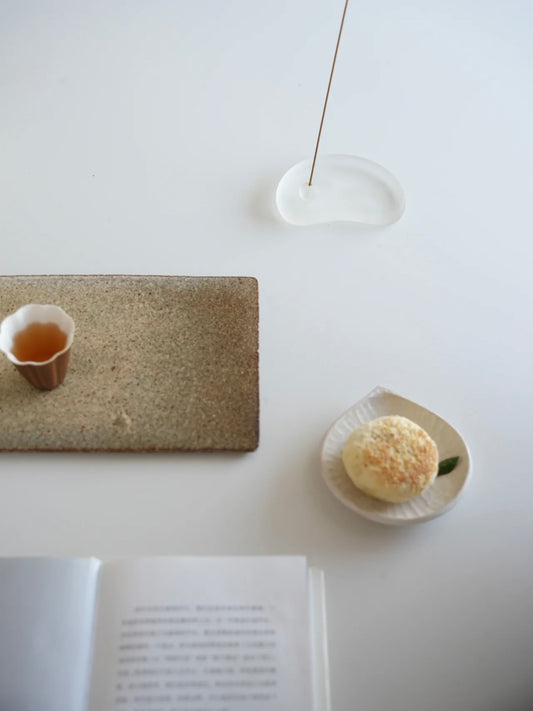 Tea cup, stone tray, and flower on a white surface with a book open.