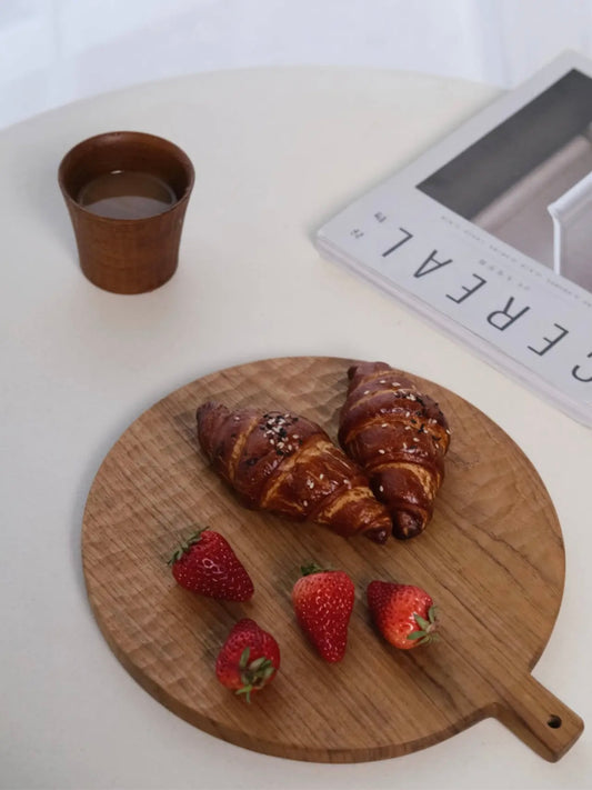 Wooden cutting board with croissants and strawberries on a white surface.