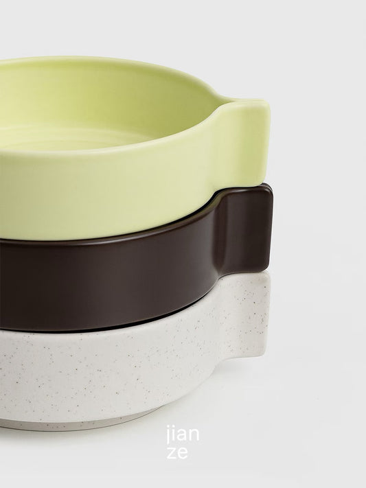 Stackable ceramic bowls in green, brown, and white on a light gray background
