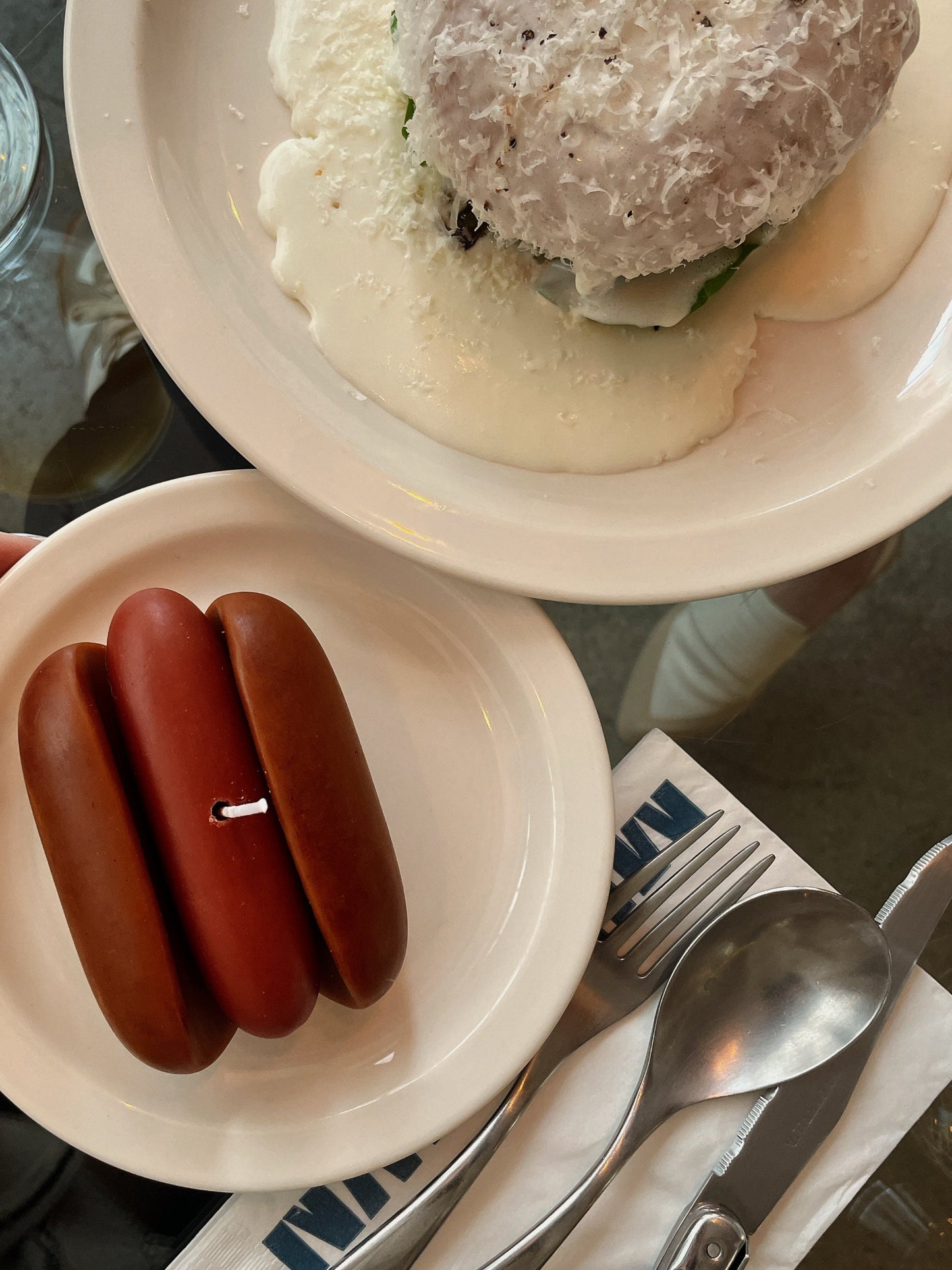 Two small brown items on a white plate with a fork and knife beside it, on a glass table.