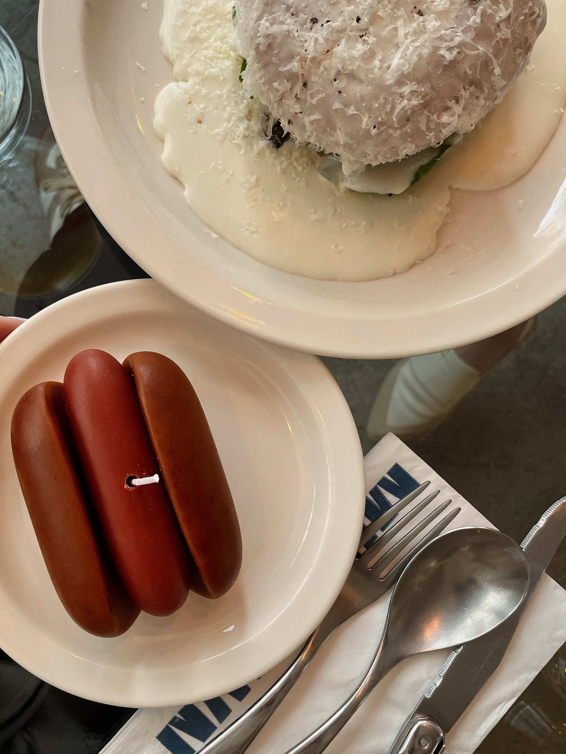 Two small brown items on a white plate with a fork and knife beside it, on a glass table.