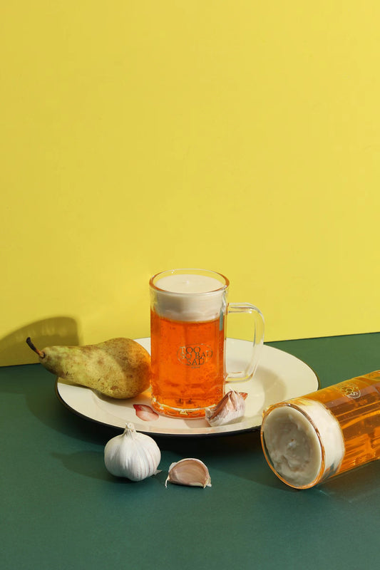 Glass of beer on a white plate with a pear and garlic cloves against a yellow background