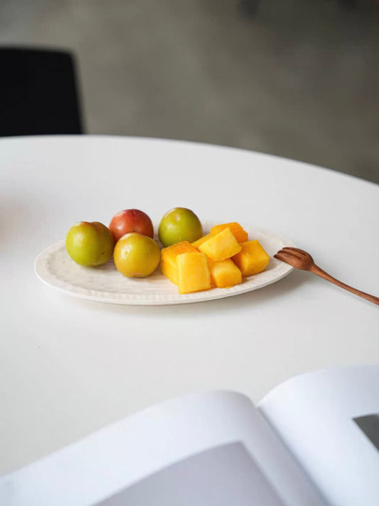 Plate of fruits including apples and mangoes on a white surface with a blurred background