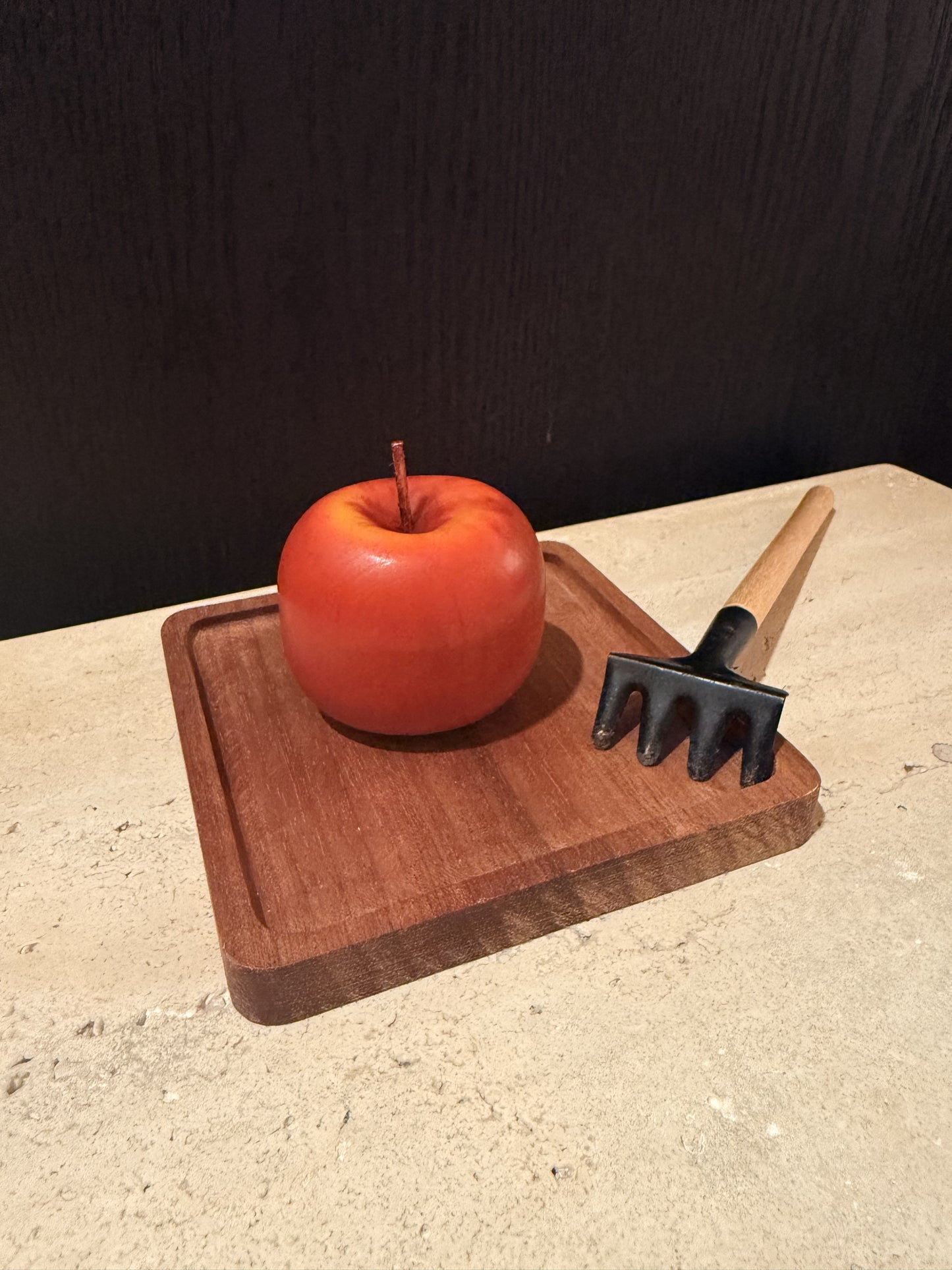 Red apple on a wooden cutting board with a black kitchen tool on a beige surface.