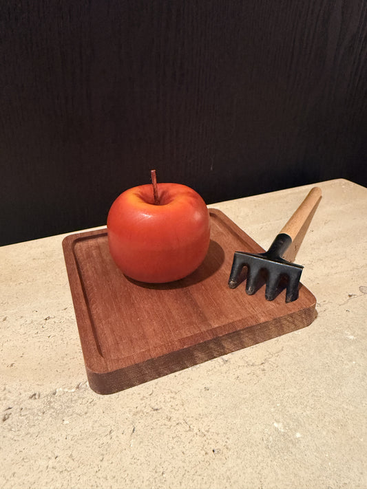 Red apple on a wooden cutting board with a black kitchen tool on a beige surface.