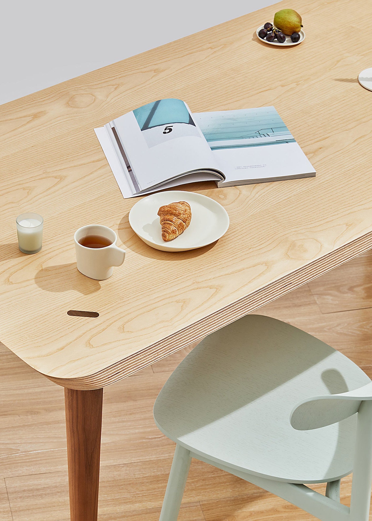 Wooden dining table with a chair, open book, and small items on a light wooden floor.