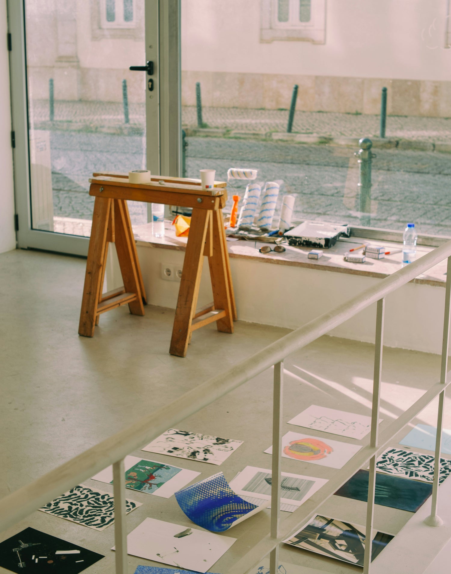 Artistic prints displayed on a glass floor with a wooden stool nearby.