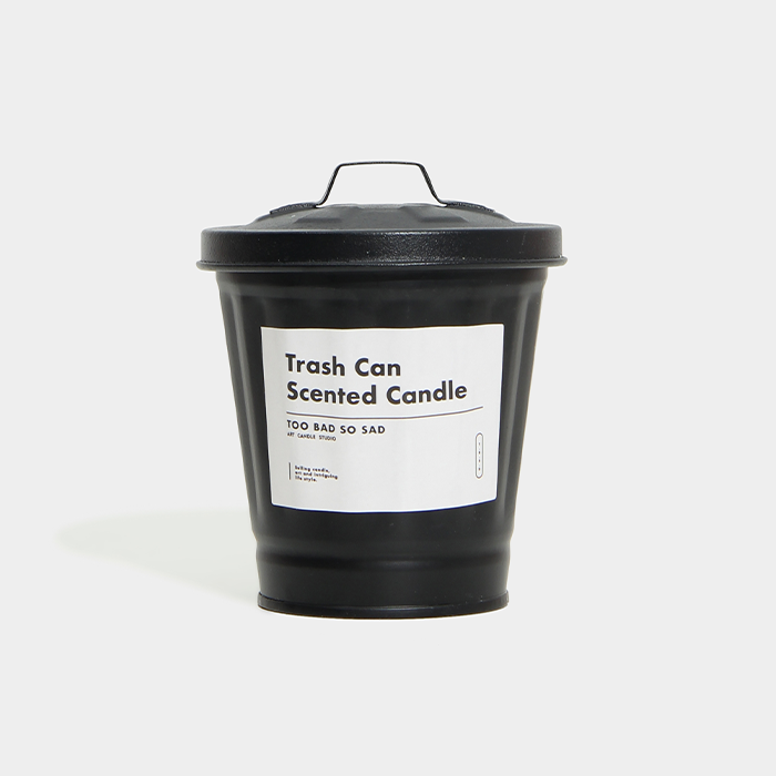 Black trash can-shaped candle with a label on a white background