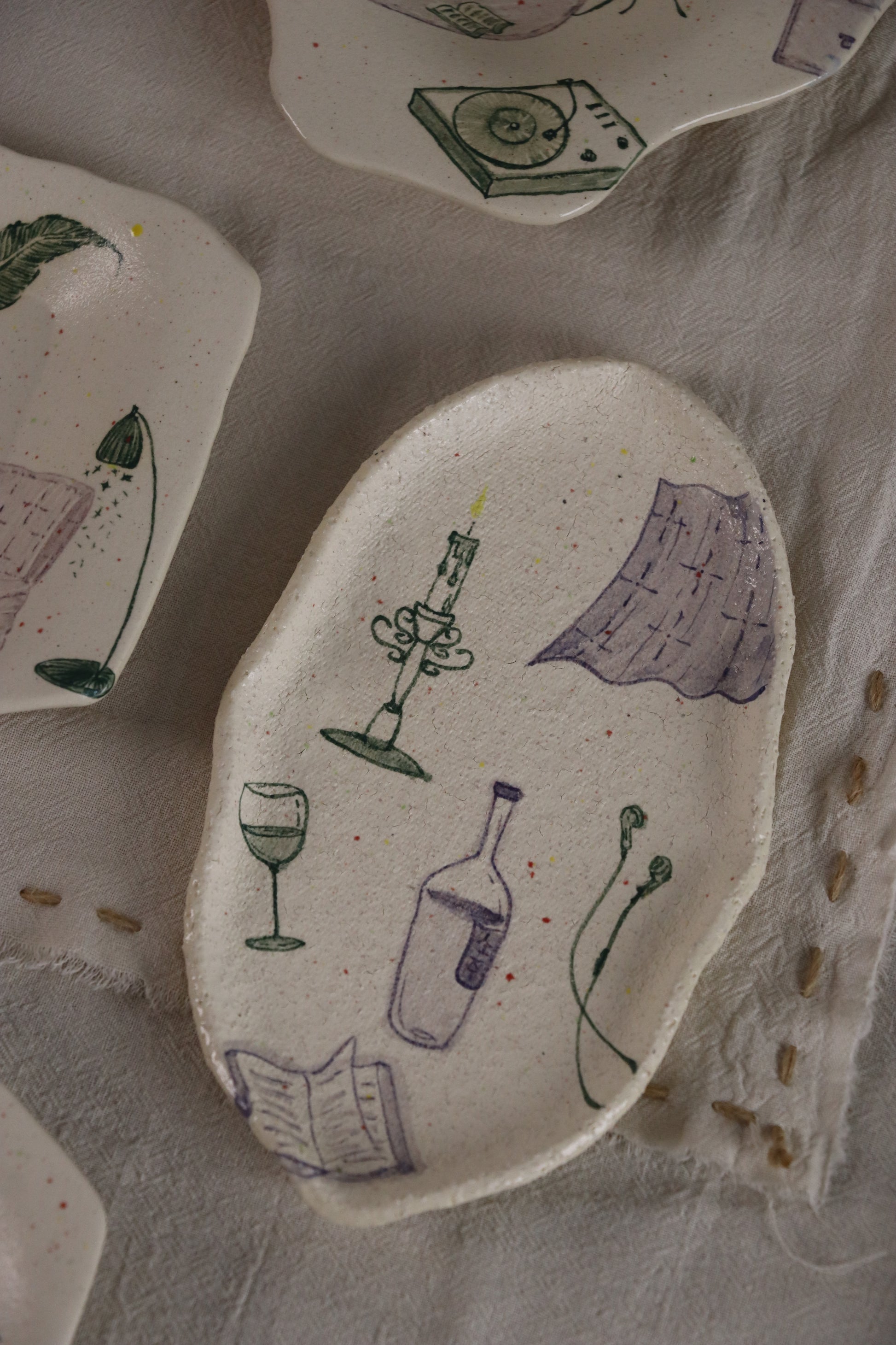 Handmade ceramic plate with wine-themed illustrations on a textured surface.
