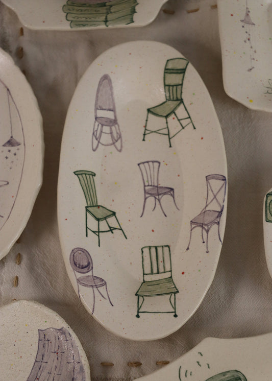 Oval-shaped ceramic plate with hand-drawn illustrations of chairs on a textured surface.