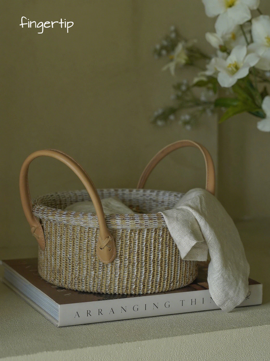 Woven basket with leather handles on a book, with white flowers in the background