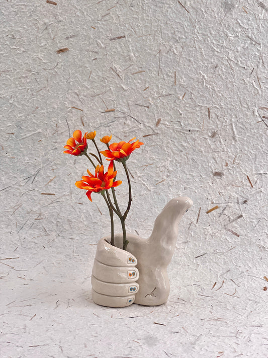 Ceramic hand-shaped vase with orange flowers on a textured gray background