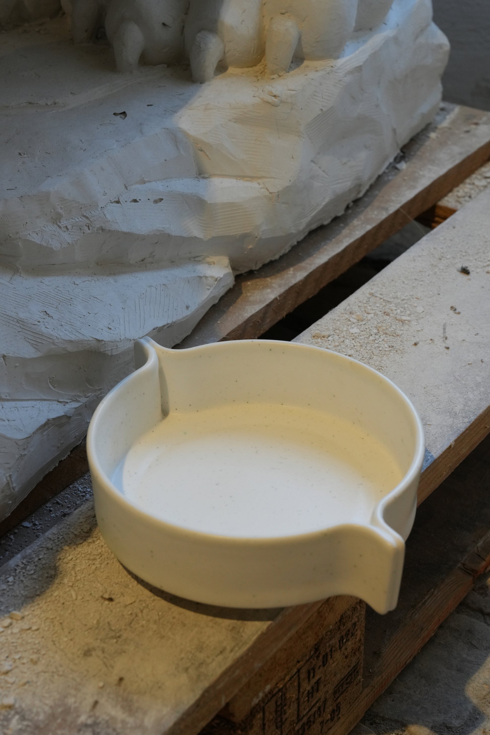 White ceramic bowl on a wooden surface with a stone sculpture in the background