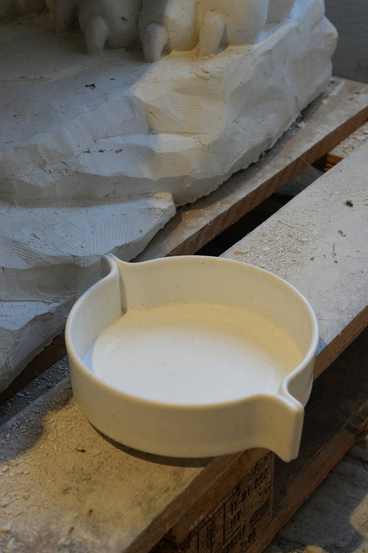 White ceramic bowl on a wooden surface with a stone sculpture in the background