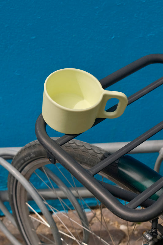 Yellow mug attached to a bicycle rack against a blue wall