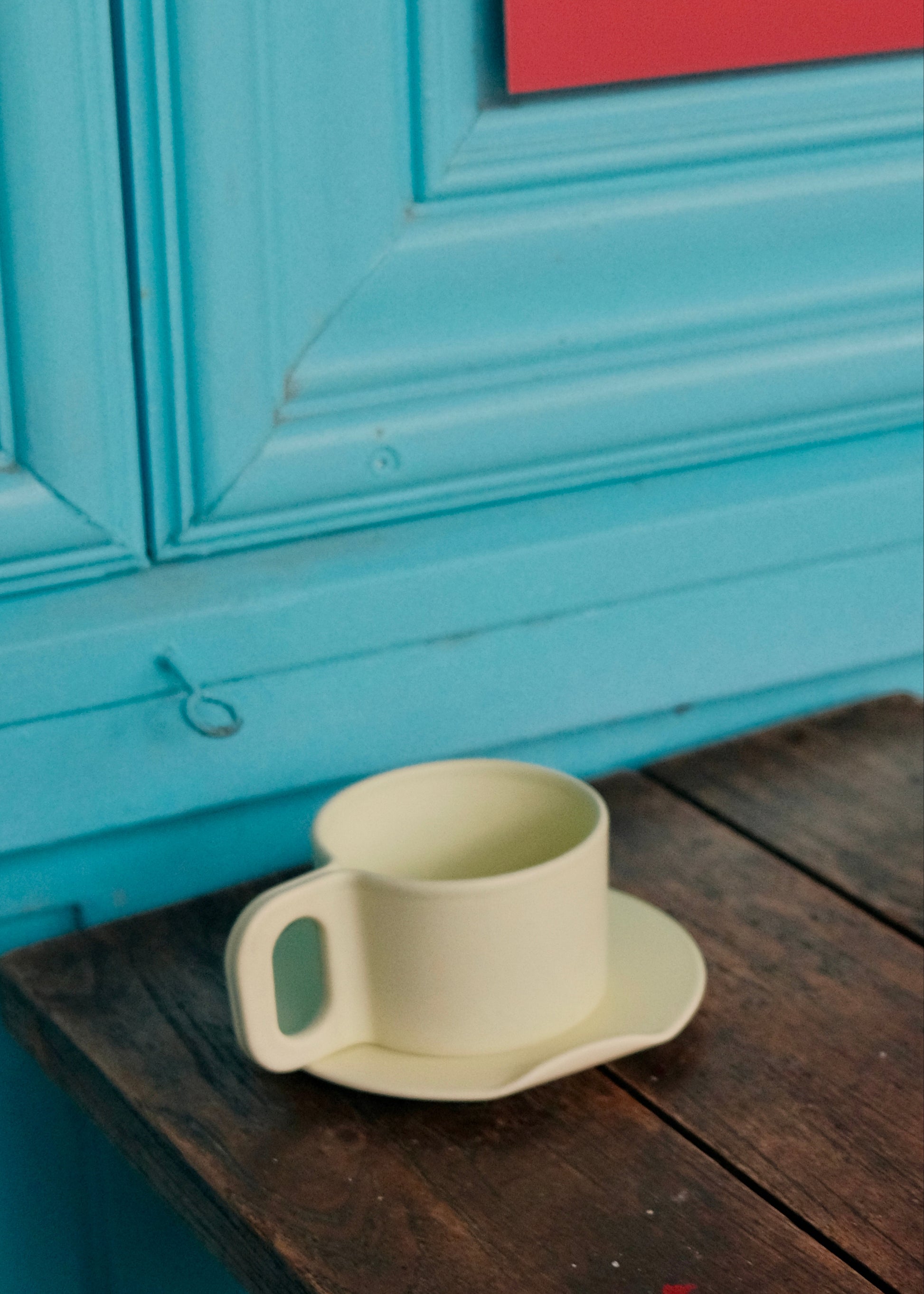 White ceramic cup and saucer on a wooden surface with a blue wall in the background