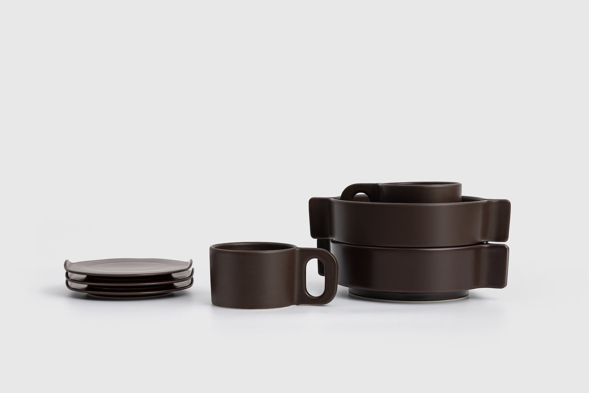 Set of dark brown ceramic dishes including plates and mugs on a light gray background