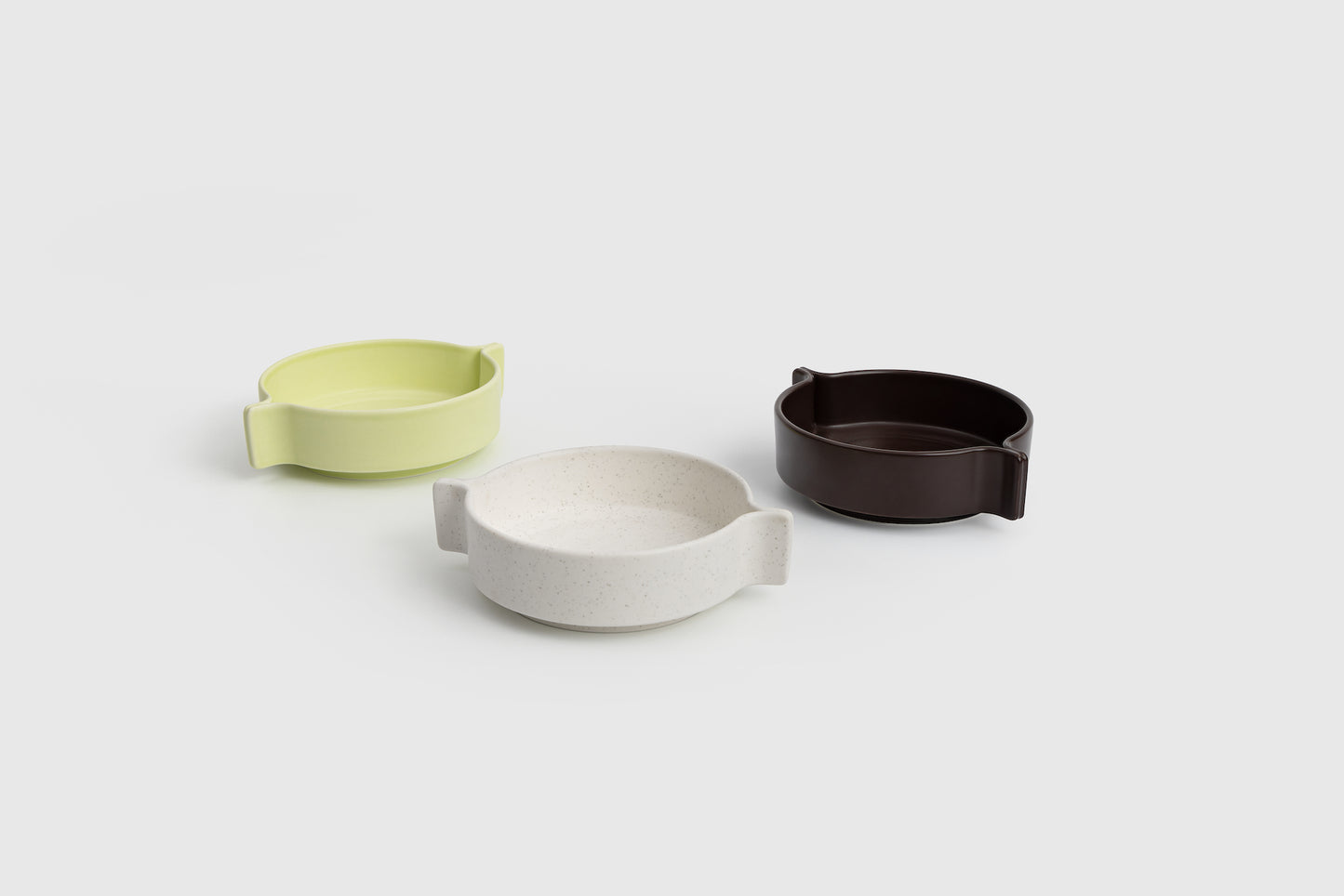 Three ceramic bowls in green, white, and brown on a light gray background