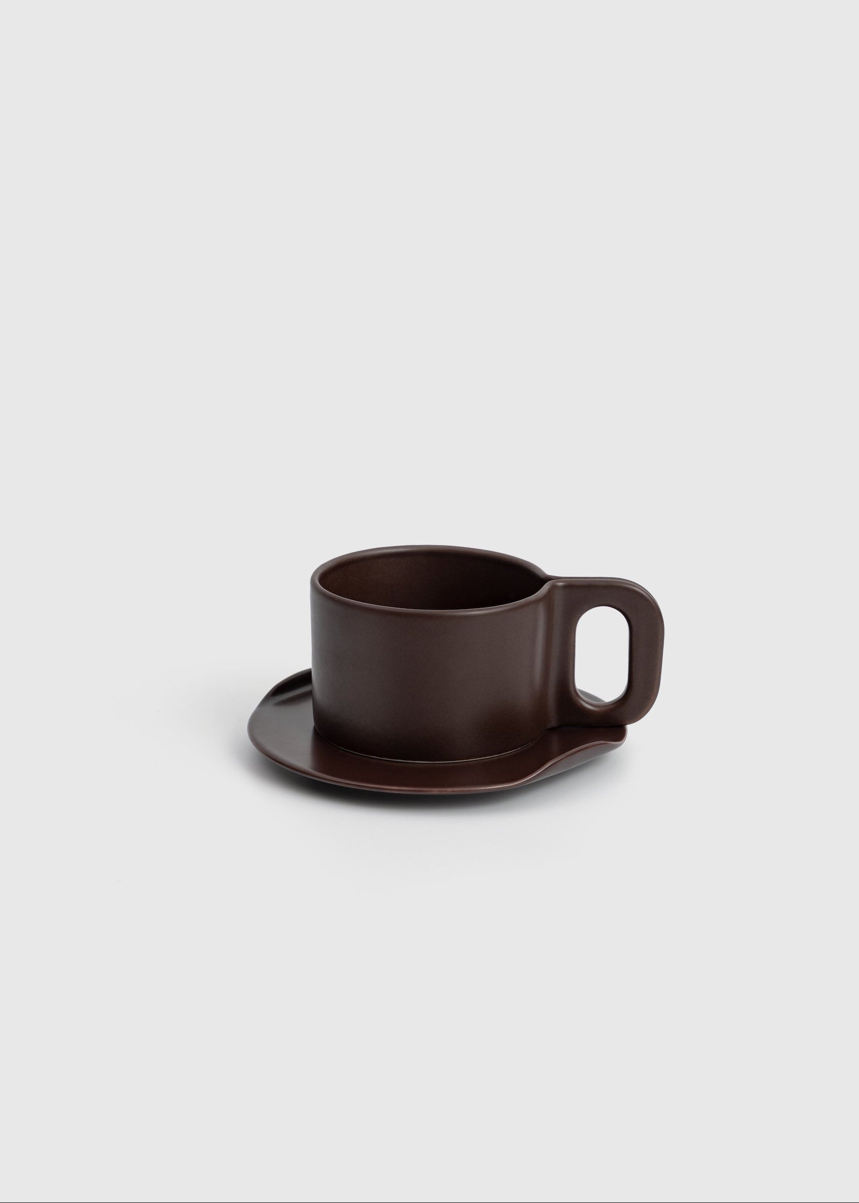 Brown ceramic cup and saucer on a light gray background