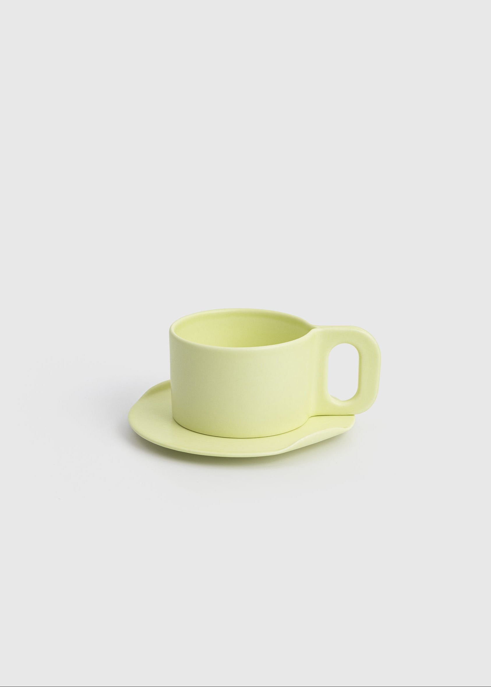 Yellow ceramic cup and saucer on a light gray background