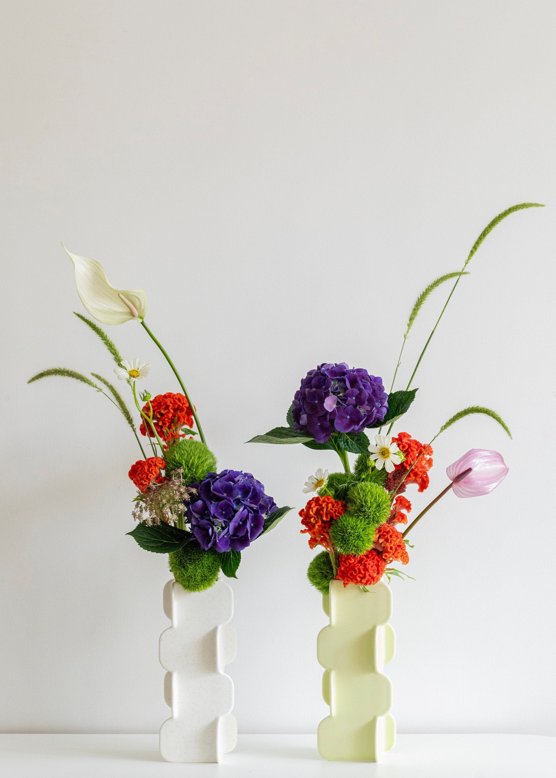 Two floral arrangements in white vases on a light background