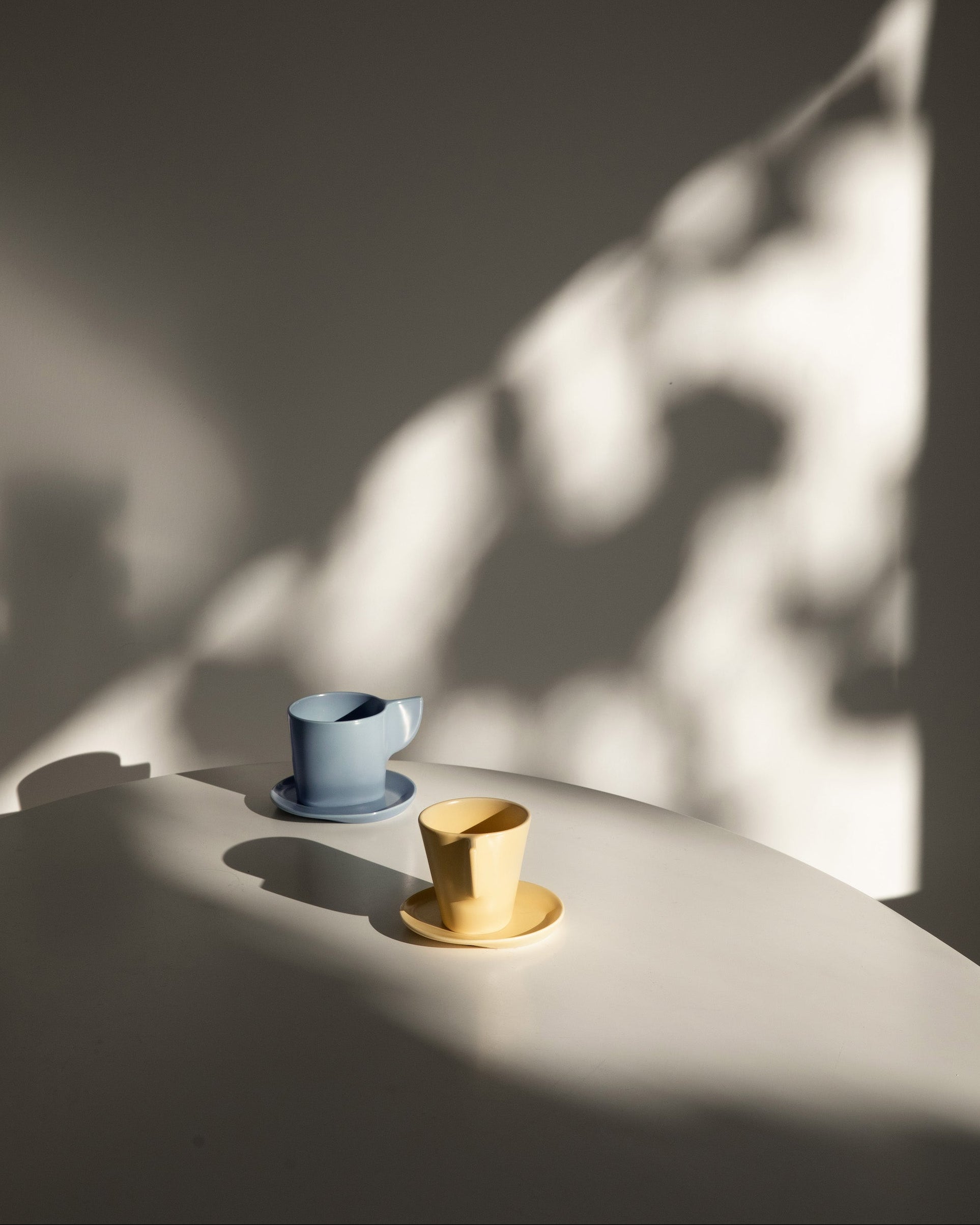 Two ceramic cups, one blue and one yellow, on a white surface with soft shadows.
