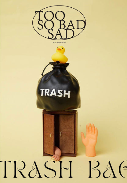 Black trash bag labeled 'TRASH' with a yellow duck and a foot emerging from it, on a beige background.